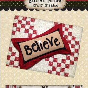 May include: A red and white checkered fabric pillow with the word "Believe" embroidered on it. The pillow is 12 inches by 17 1/2 inches and is finished. The image also includes a sign that says "My Red Door Designs".