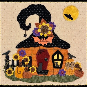 May include: A whimsical Halloween-themed applique featuring a witch's hat atop an orange house with a black door and window. Sunflowers, pumpkins, and a full moon with a bat add to the festive scene. The text "The Critter Corner" is visible.