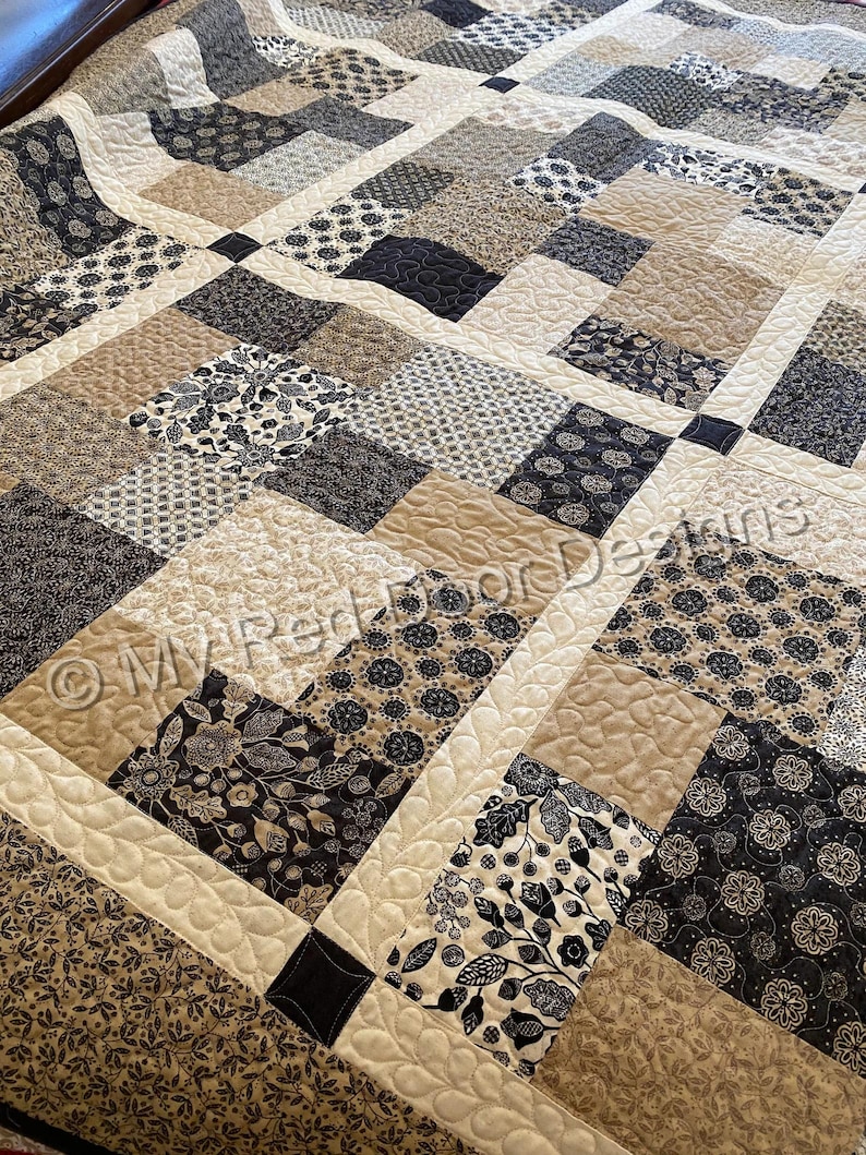Op de afbeelding: Een patchwork quilt met een herhalend patroon van vierkante blokken in tinten zwart, cr&egrave;me en beige. De stoffen vierkanten tonen diverse bloemen-, blad- en geometrische prints, verbonden door cr&egrave;mekleurige tussenstroken met een doorgestikte textuur.