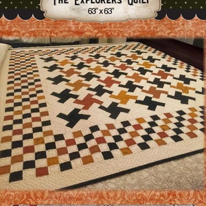 Puede incluir: La colcha "The Explorers Quilt", una colcha de 63" x 63" con un patrón geométrico negro, marrón y naranja. La colcha está hecha con un fondo blanco y tiene un borde negro. La colcha se muestra en una cama con una colcha de estampado floral rojo y naranja.