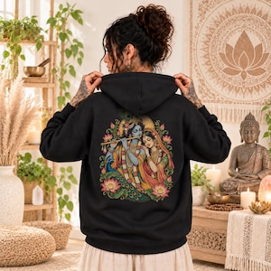 May include: A black hooded sweatshirt featuring a detailed, colorful graphic on the back. The illustration depicts the Hindu deities Krishna and Radha, with Krishna playing a flute, surrounded by lotus flowers and a peacock feather motif.