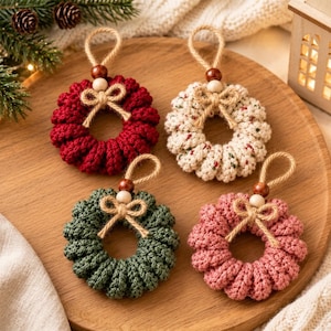 May include: Four circular crochet ornaments in red, cream with speckles, dark green, and dusty pink. Each wreath features a jute twine hanging loop, a dark brown wooden bead, a light wooden bead, and a small tied jute twine bow.