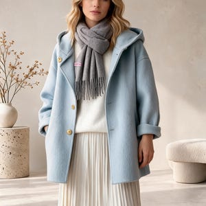 May include: A light blue hooded coat with large buttons, worn over a white sweater and a white pleated skirt. A grey scarf with fringe detail is wrapped around the neck. The coat features long sleeves with folded cuffs and a structured hood.