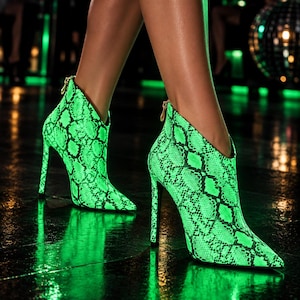 May include: A pair of neon green and black snakeskin print ankle boots with a pointed toe, a high stiletto heel, and a gold-toned zip pull at the back. The boots feature a deep V-cut opening at the ankle and a textured reptilian pattern.