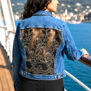 May include: A blue denim jacket featuring a large, sheer back panel adorned with intricate black floral embroidery. The jacket includes a classic collar, long sleeves, and metal button closures along the front and at the cuffs, providing a structured fit.