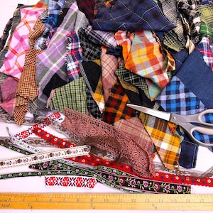 May include: A collection of assorted fabric scraps in various plaid, checkered, and solid patterns, alongside several decorative ribbons with floral and geometric designs, a pair of metal scissors, and a wooden ruler measuring 19 inches.