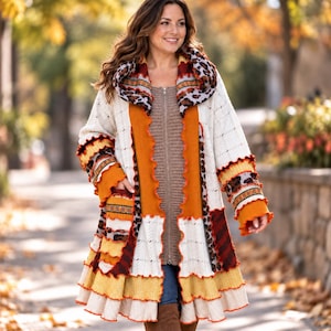 May include: A long, open-front cardigan featuring a patchwork design with cream, mustard yellow, burnt orange, and brown tones. The garment includes a large hood, ruffled trim along the edges, and a mix of cable knit and leopard print patterns.