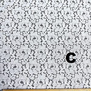 May include: White lace fabric with a floral pattern. A wooden ruler with inch markings is at the bottom. A black letter "C" is in the center. The fabric has a delicate, open weave design.