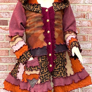 May include: A multi-colored patchwork jacket with a hood, featuring a leopard print, brown, orange, and pink fabric. The jacket has a button closure and a ruffled hem.