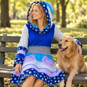 Puede incluir: Un vestido con capucha que presenta un diseño de patchwork con secciones en azul, azul claro y gris. La tela incluye un patrón de huellas blancas, paneles en azul sólido, mangas de punto trenzado gris y detalles de encaje de ganchillo lavanda.