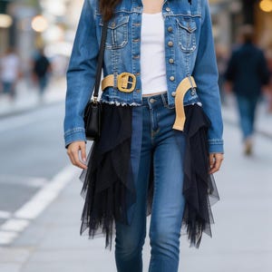Könnte beinhalten: Eine Frau trägt eine Jeansjacke mit schwarzen Spitzendetails, ein weißes Oberteil und eine blaue Jeans. Sie trägt auch einen schwarzen Tüllrock, einen beigen Gürtel mit goldener Schnalle, eine schwarze Handtasche und silberne Ballerinas. Das Outfit ist für einen lässigen Look gestylt.