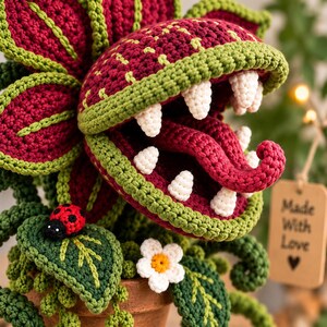 May include: A crocheted Venus flytrap plant in a terracotta pot, featuring deep red and green yarn petals, white teeth, and a red tongue. A small red and black ladybug and a white flower are attached. A tag reads Made With Love.