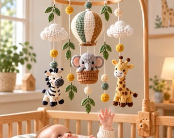 May include: A nursery mobile featuring crocheted figures of a zebra, a giraffe, and an elephant in a hot air balloon, suspended from a wooden ring with white clouds, green leaves, and yellow and green spheres on white strings.
