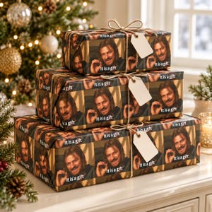 May include: Three stacked rectangular gift boxes wrapped in custom paper featuring a repeating photographic print of a man with long brown hair and the text It is a gift. Each box is tied with natural jute twine and a blank white gift tag.