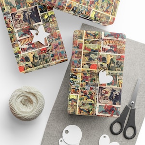 May include: Rectangular gifts wrapped in colorful comic book paper featuring Spider-Man illustrations and the text RAKASH. Each package is tied with brown twine and includes a white star or heart-shaped gift tag for labeling.