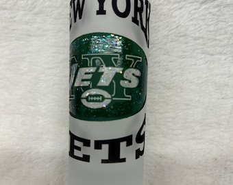 May include: A frosted glass shot glass with a green, white, and black New York Jets logo. The logo includes the words "New York Jets" and a football.