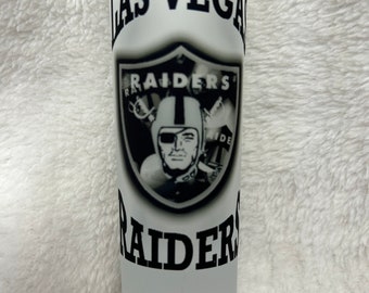 Puede incluir: Un vaso de chupito blanco esmerilado con un logotipo negro y blanco de los Las Vegas Raiders. El logotipo presenta un escudo negro con las palabras "Raiders" en un círculo blanco y una imagen en blanco y negro de la cara de un jugador de fútbol.