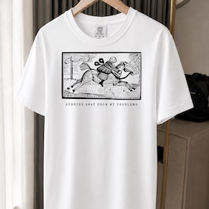 Może przedstawiać: Biały t-shirt z krótkim rękawem z czarną grafiką w stylu tuszu przedstawiającą osobę jadącą konno. Pod ilustracją znajduje się napis RUNNING AWAY FROM MY PROBLEMS prostą czcionką wielkimi literami. Koszulka posiada okrągły dekolt.