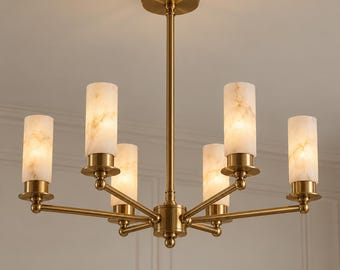 May include: A brass chandelier featuring a central rod and five horizontal arms, each supporting a cylindrical, white, marble-patterned glass shade. The fixture is finished in a warm metallic tone and includes a circular ceiling canopy mount.