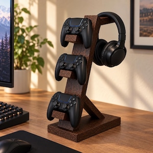 May include: A dark brown wooden stand featuring three horizontal shelves for holding gaming controllers and a curved top arm designed to support a pair of black over-ear headphones. The stand has a rectangular base and a slanted vertical support.