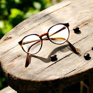 May include: Tortoise shell eyeglasses with round lenses on a wooden surface.