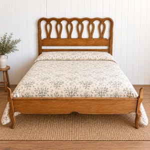 May include: A wooden bed frame with a high headboard featuring a series of vertical, rounded cutouts. The bed is dressed in a cream-colored quilt with a repeating dark green botanical pattern of small trees and branches across the entire surface.