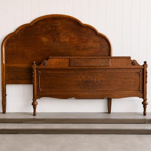 May include: A disassembled antique wooden bed frame with a tall, scalloped headboard and a footboard. The bed frame is a warm brown color, with decorative carvings and two metal side rails.