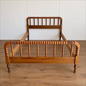 May include: A wooden bed frame featuring a headboard and footboard with a spindle design. The frame is constructed from light brown wood with a smooth finish, showcasing a series of vertical turned spindles and horizontal rails.
