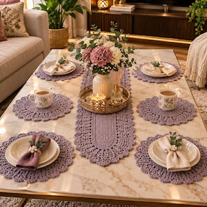 May include: A set of lavender crochet placemats and a matching table runner on a marble table. The arrangement includes white plates with folded napkins, floral mugs, and a gold tray holding a vase of pink and white flowers with a candle.