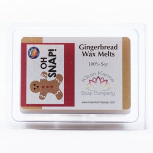 Op de afbeelding: Een doorzichtige plastic container met een label waarop "Gingerbread Wax Melts" en "100% Soy" staat. Het label bevat ook een afbeelding van een peperkoekman en de tekst "Oh Snap!" en "Klean Karma Soap Company".