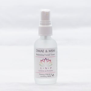 May include: A clear glass bottle with a white spray top and label. The label reads "DMAE & MSM Balancing Facial Toner" with a pink and purple lotus flower graphic. Below the flower is the text "LNP LOTIONS & POTIONS" and "Firming DMAE & soothing MSM".