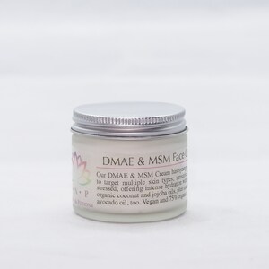 May include: A silver jar with a white label that reads "DMAE & MSM Face Cream". The label describes the cream as having a synergistic blend of ingredients to target multiple skin types, including sensitive and stressed skin. It also mentions that the cream offers intense hydration with organic coconut and jojoba oils, plus avocado oil. The label states that the cream is vegan and 75% organic.