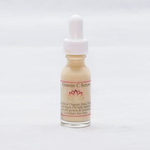 May include: A clear glass bottle with a white dropper top and a label that reads "Vitamin C Serum". The label also features a pink lotus flower and text describing the serum's ingredients and benefits.
