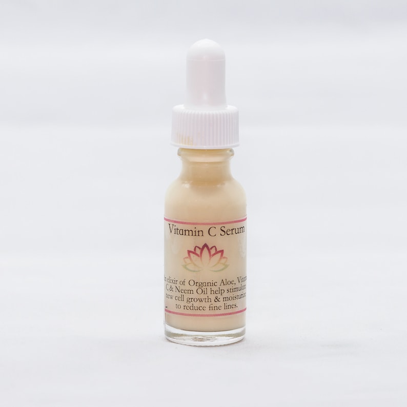 May include: A clear glass bottle with a white dropper top and a label that reads "Vitamin C Serum". The label also features a pink lotus flower and text describing the serum's ingredients and benefits.