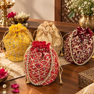 May include: Four drawstring pouches in yellow, beige, red, and maroon, each featuring a lattice pattern of gold metallic trim and embedded circular mirrors. The bags have beaded handles and a gathered top closure with matching drawstring cords.