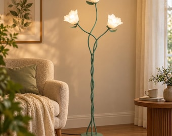 May include: A floor lamp with a green metal base and stem featuring three intertwined branches. Each branch ends in a white, frosted glass shade shaped like a flower blossom. The lamp emits a warm, soft glow from the three illuminated bulbs.