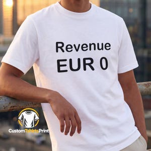 Op de afbeelding: Een wit T-shirt met korte mouwen en de zwarte tekst "Revenue" op de bovenste regel en "EUR 0" op de onderste regel. Het shirt heeft een ronde hals en een standaard pasvorm, met de tekst duidelijk gedrukt in het midden van de borst.