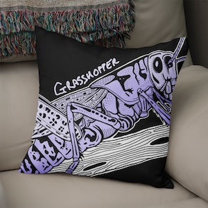 May include: A black pillow featuring a purple and white illustration of a grasshopper. The text "Grasshopper" is written in white on the pillow.
