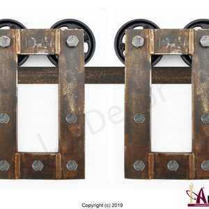 May include: Two rectangular metal barn door hangers featuring a weathered brown finish and exposed silver bolts. Each hanger is stamped with the year 1925 and includes two black circular wheels positioned on a horizontal metal track rail.