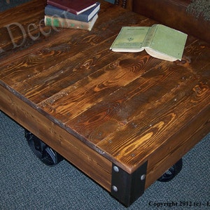 May include: A rustic wooden coffee table with a distressed brown finish. The table is on wheels and has metal accents. A book is on top of the table.