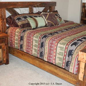 May include: A rustic wooden bed frame and matching nightstand. The bed has an X-shaped headboard. The bedding features a pattern of bears, trees, and geometric shapes in brown, green, and red. A lamp sits on the nightstand, with the bed frame and nightstand made of wood.
