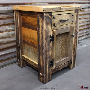 May include: A rustic wooden nightstand with a single drawer and a cabinet door. The nightstand is made from reclaimed wood and has a distressed finish. The drawer has a black metal handle and the cabinet door has black metal hinges.
