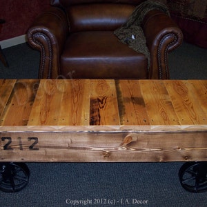 May include: A rustic wooden coffee table with a reclaimed wood top and black metal wheels. The table has a distressed finish and features the number "212" printed on the front.