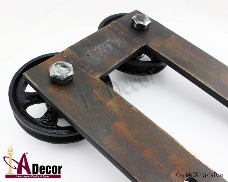 May include: A U-shaped metal bracket with a rusted finish, featuring two black spoked wheels attached by silver hexagonal bolts. The metal surface is stamped with the number 1776. The bracket has a flat, rectangular frame design.