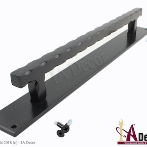 May include: A black door pull handle with a textured grip and a rectangular base. The handle is accompanied by screws for installation. The text "IA Decor" is visible on the base.
