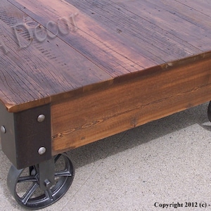 May include: A rustic wooden coffee table with a dark brown finish. The table has a square top and is supported by four black metal wheels. The table is made of reclaimed wood and has a distressed look. The table is perfect for adding a touch of industrial style to any living room.