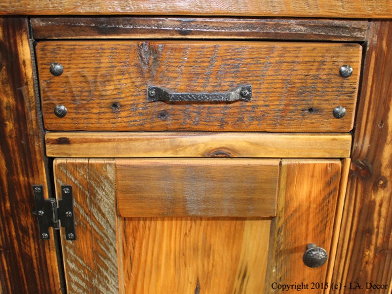 May include: Close-up of a wooden cabinet with a drawer and a door. The drawer has a black metal handle and the door has black metal hinges. The wood is a rustic brown color with a natural finish.
