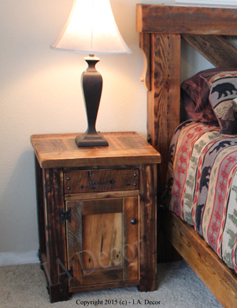 May include: A rustic wooden nightstand with a single drawer and a door. The nightstand is made of reclaimed wood and has a dark brown finish. It features a simple design with a single drawer and a door. The nightstand is sitting next to a bed with a rustic wooden headboard.