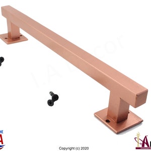 May include: A brushed rose gold door handle with square ends and a T-shaped design. The handle is made of metal and comes with two black screws.