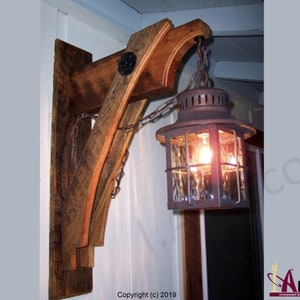 May include: A rustic wooden wall sconce with a metal lantern hanging from it. The lantern has a glass shade and a light bulb inside. The sconce is attached to the wall with screws. The lantern is hanging from a chain. The sconce is made of reclaimed wood. The lantern is made of metal. The sconce is a great way to add a rustic touch to any home.